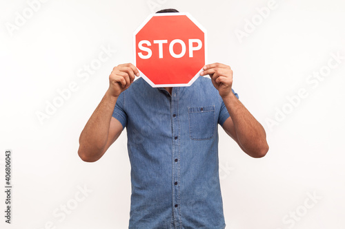 Scared man in blue shirt hiding face behind stop sign, victim of bullying, violence and discrimination. Indoor studio shot isolated on white background