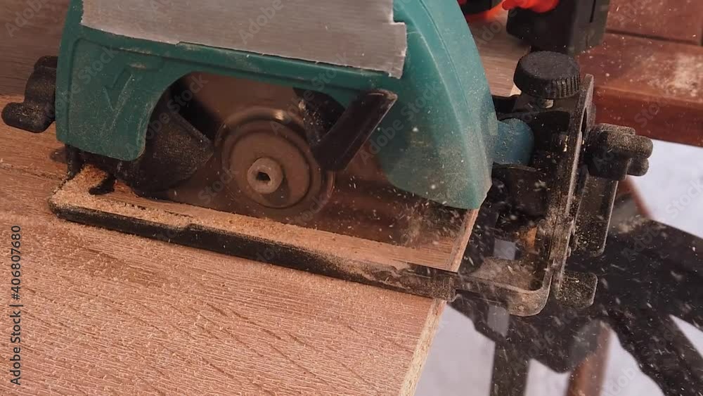 A male worker saws a wooden panel on a table using a circular disc on a radiator.