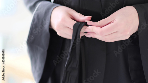 Close-up woman in black silk robe ties belt on her robe.