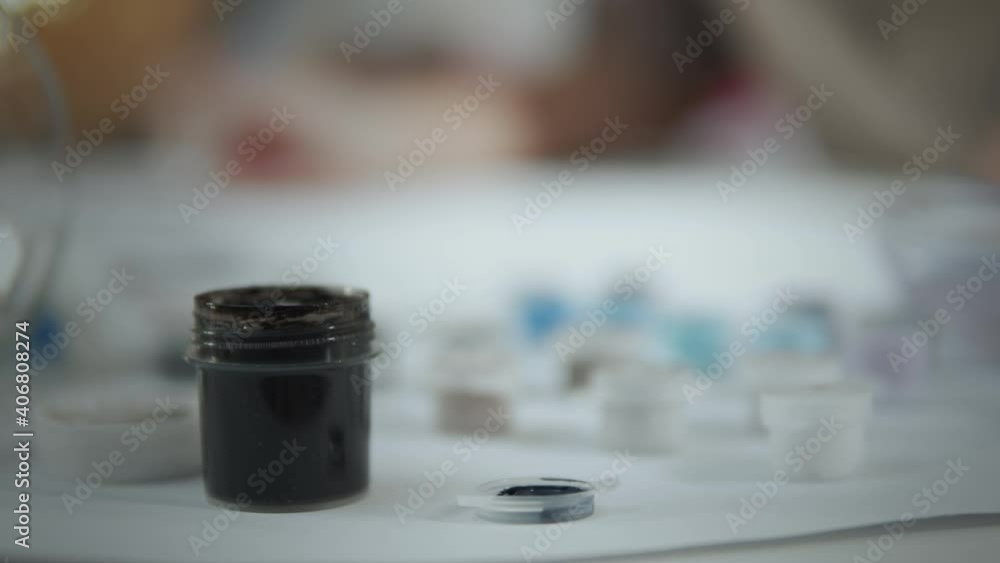 Crop of artist hand putting paintbrush in black color. Woman Painting With Gouache Indoors. Artist picking up colors from painter palette. Crop of artist hand putting paintbrush in black color. Woman Painting With Gouache Indoors. Artist picking up colors from painter palette.