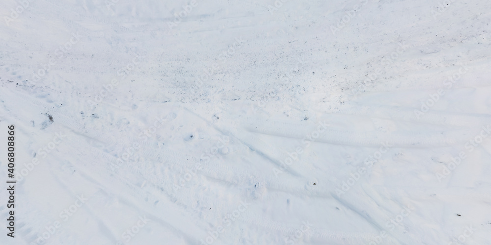 panorama view from above on texture of snow covered road with car tire tracks and footprints