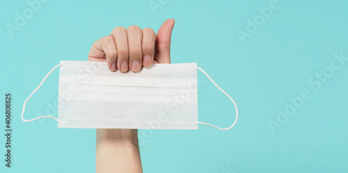 Hands holding white surgical face mask on green or Tiffany Blue background.