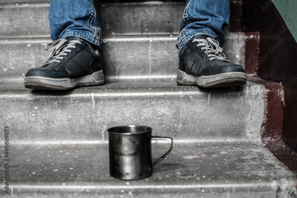 a metal mug stands on a concrete staircase stands, in the background a homeless man a metal mug stands on a concrete staircase stands, in the background a homeless man