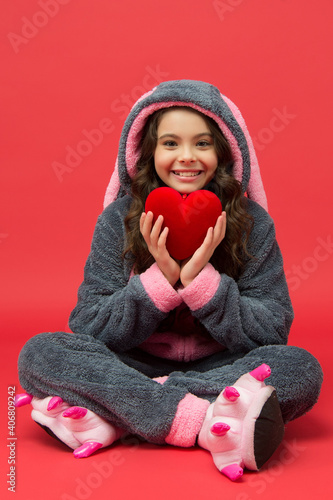 Happy kid hold big red valentines heart sitting in cosy pajamas, cardiovascular photo