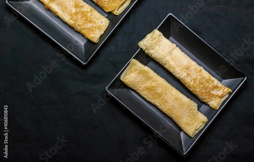 Bengali sweet - Patishapta Pitha in a black plate on isolated black background, a traditional Bengali pancake recipe where the pancakes are stuffed with kheer or coconut. photo
