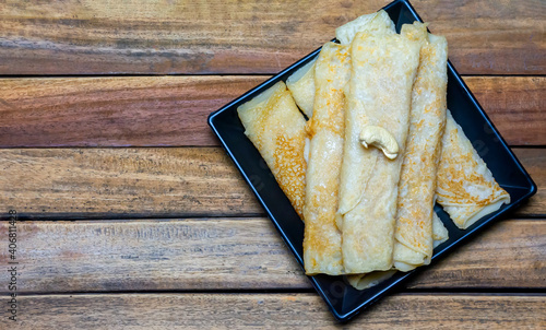 Bengali sweet - Patishapta Pitha in a black plate on wooden background, a traditional Bengali pancake recipe where the pancakes are stuffed with kheer or coconut.