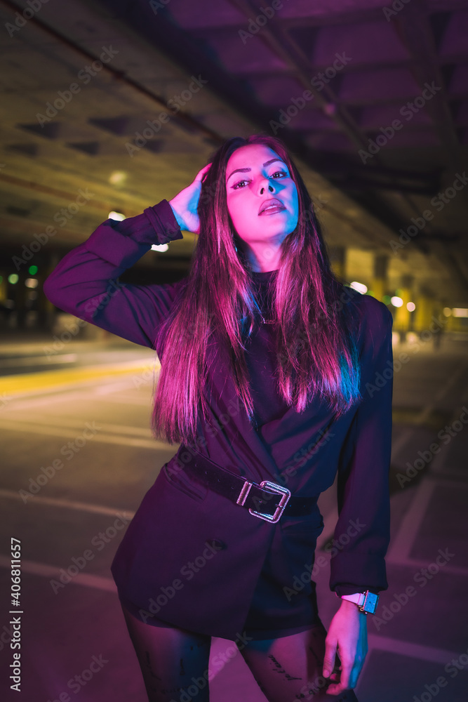 Portrait of young brunette Caucasian model at night in an underground parking lot, illuminated with neon