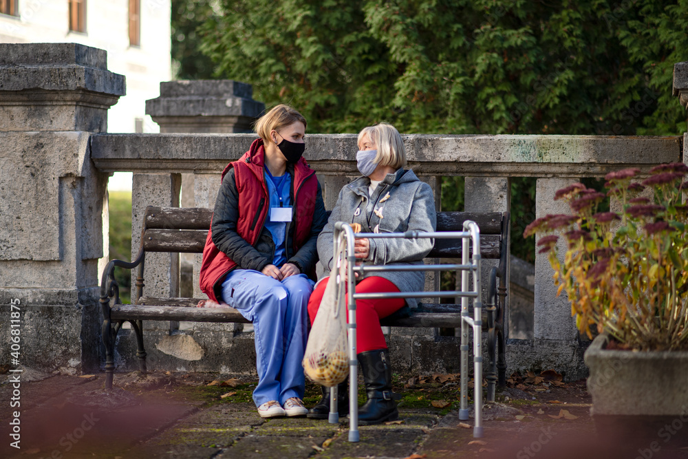 Obraz premium Senior woman with walking frame and caregiver outdoors sitting in park, coronavirus concept.