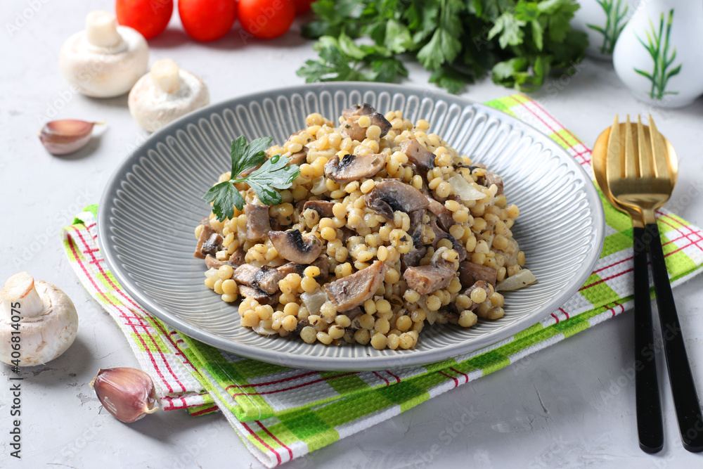 Homemade ptitim pasta with champignons in a plate on light gray table. Horizontal format. Homemade ptitim pasta with champignons in a plate on light gray table. Horizontal format.
