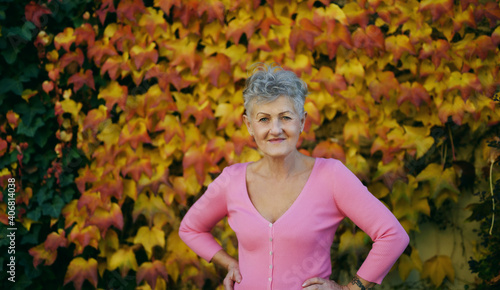 Senior woman standing outdoors against colorful natural autumn background, looking at camera.