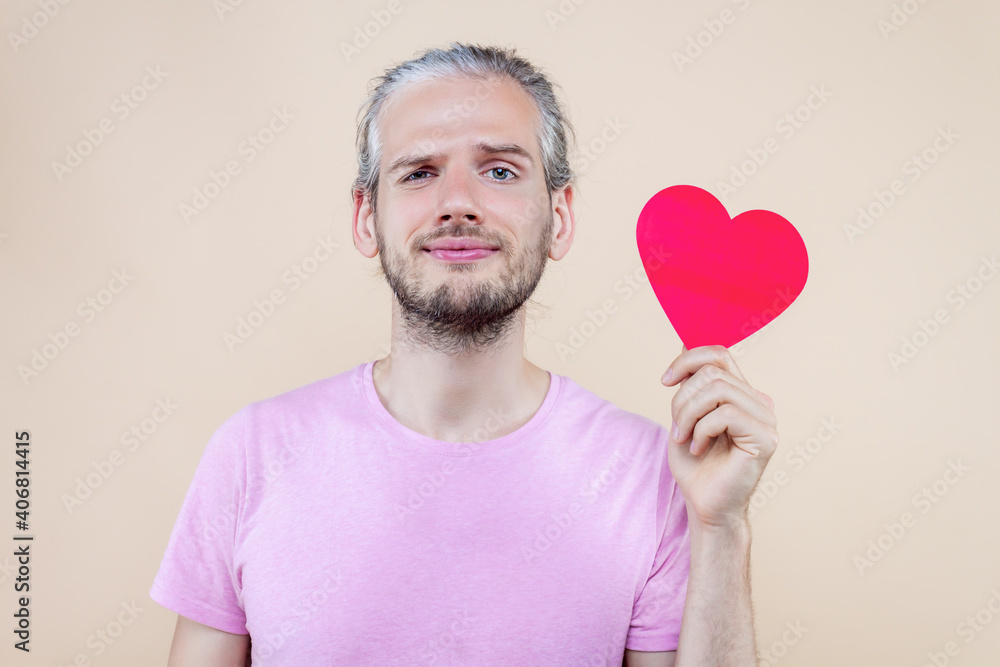 Cute smiling boy is holding red decorative sign of heart. Young man cupid in pink t-shirt is expressing sympathy, feelings. Happy St. Valentine's Day. Fall in love. Like concept. Cute smiling boy is holding red decorative sign of heart. Young man cupid in pink t-shirt is expressing sympathy, feelings. Happy St. Valentine's Day. Fall in love. Like concept.