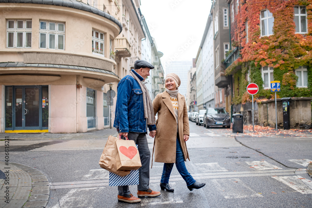 Happy senior couple walking outdoors on street in city, carrying shopping bags.