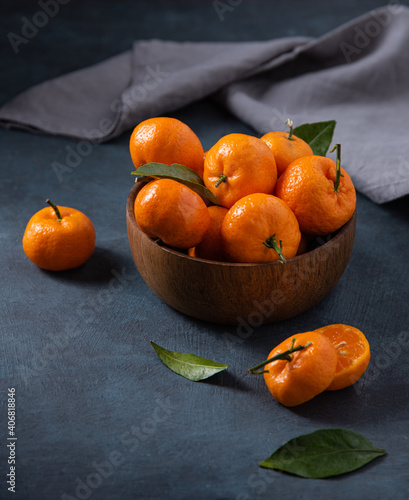 sweet tangerines with green leaves in wooden bowl  on a dark blue background with gray napkin