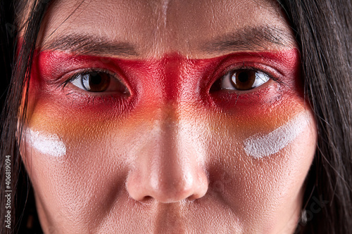 close-up eyes of indian woman confidently looking at camera, serious ethnic female with paintings on face. indian ehnicity, shaman concept photo