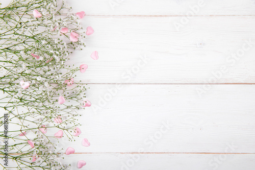 Small white flowers with pink hearts on a white wooden background, Valentines Day or Mother Day festive flat lay, space for text