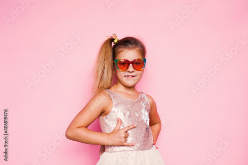 Girl with long hair in festive paper hat and dressy dress on pink background tossing gold confetti © Lena May