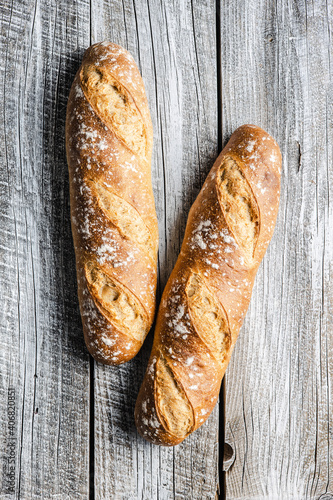 Two crispy fresh baguettes on wooden table.