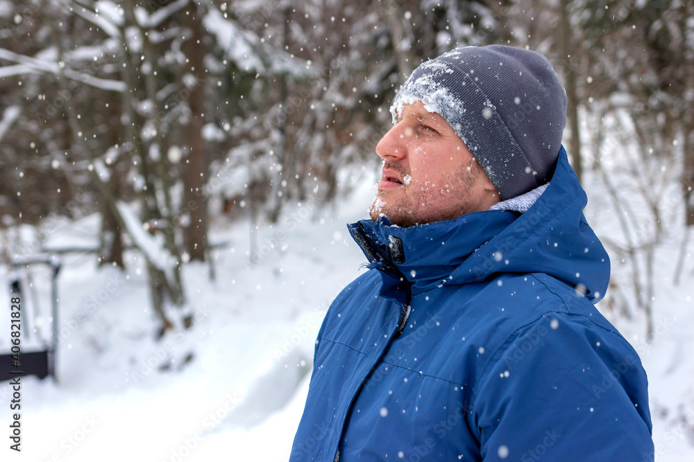 Obraz premium Portrait of a young man out in nature during snowy day in winter. Shot of a man wearing a winter coat standing in a snowy landscape. Photo of a young man with beard standing in the snowy mountains.
