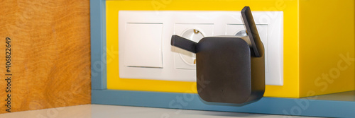 WiFi repeater in an electrical outlet on a yellow wall. An easy way to extend your wireless network at home