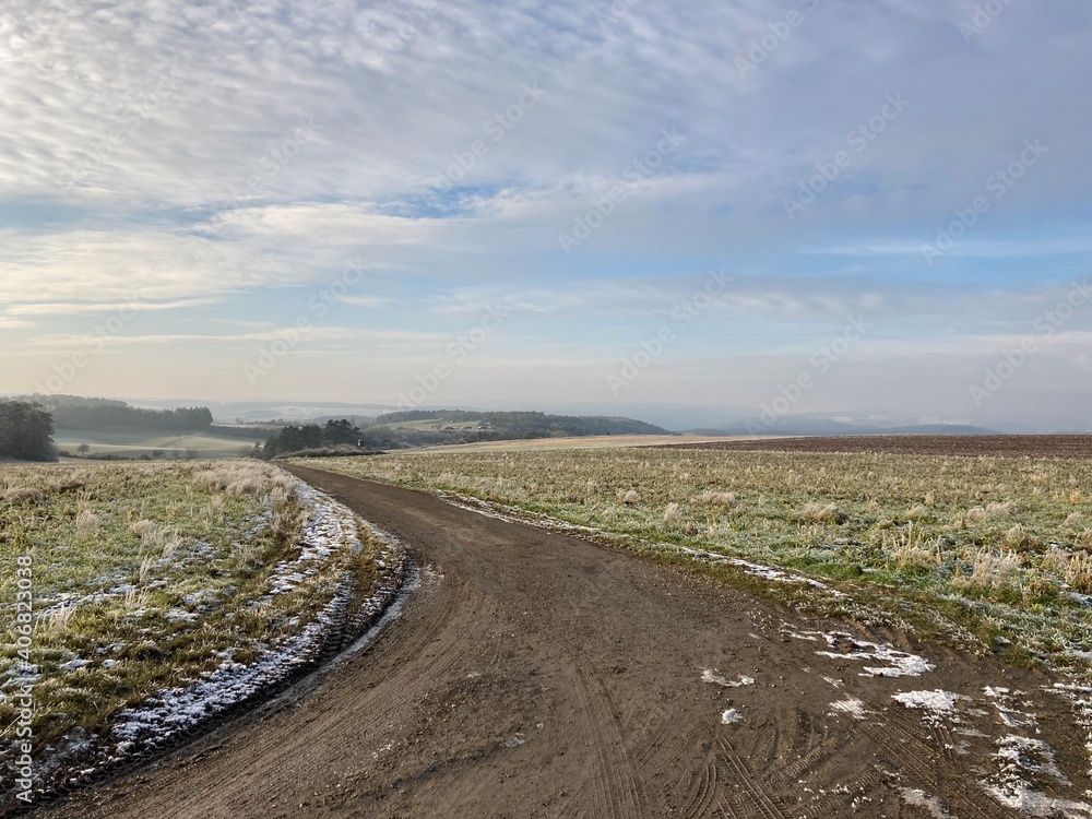 Fototapeta premium snow melting on a wide field on a sunny winters day with some clouds