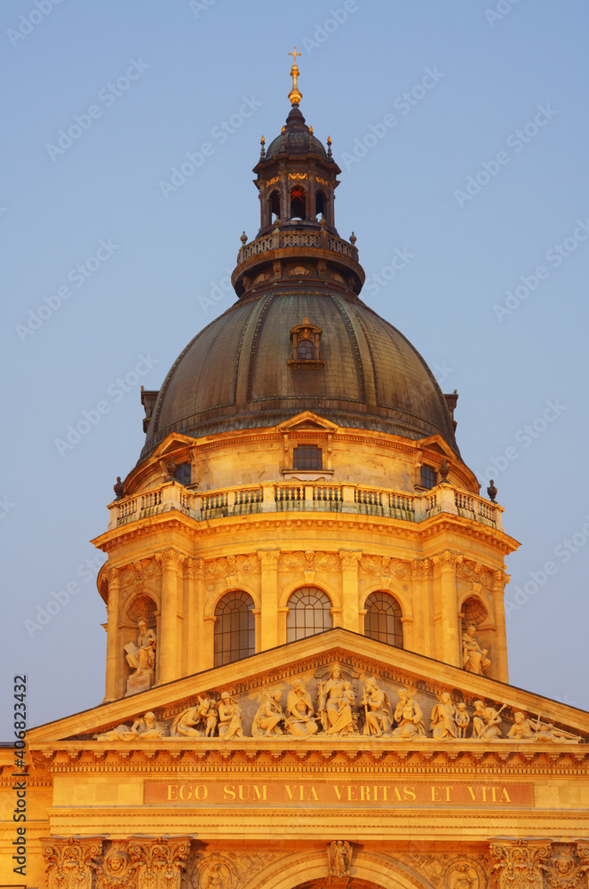 Dome and tympanum of the St. Stephen's Basilica facade, decorated with christian themed statues lit by yellow light just after sunset, Budapest, Hungary