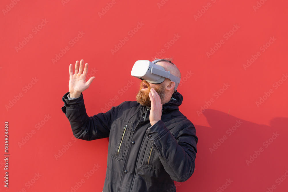 Emotional portrait of a man on the street wearing reality glasses against the background of a red wall Emotional portrait of a man on the street wearing reality glasses against the background of a red wall