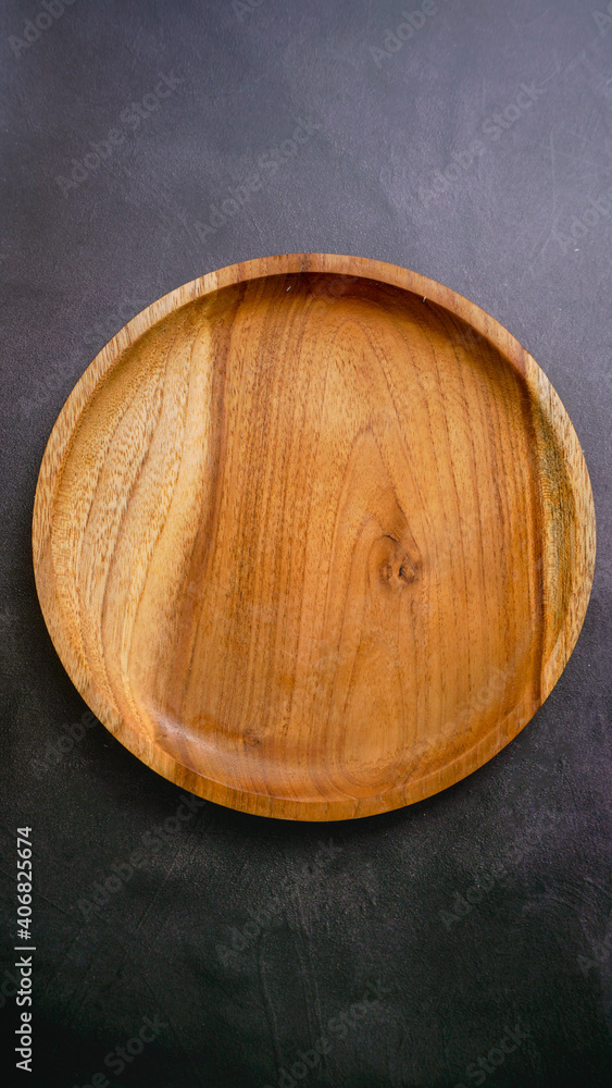 wooden empty plate on a dark stone background, a blank for design. wooden empty plate on a dark stone background, a blank for design.