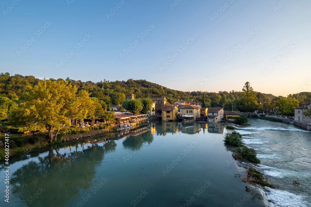 Panorama from the top of the medieval tower on the Mincio river with the waterfalls and the medieval village of Valeggio sul Mincio on a summer day, towards sunset. Verona, Veneto, Italy