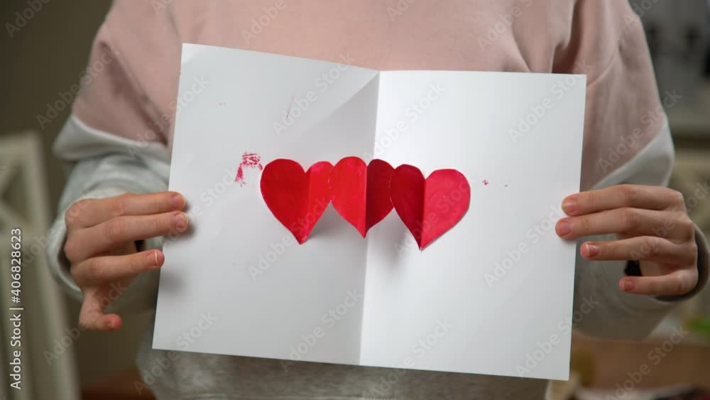 Hands unfolding handmade greeting card for Valentines day. I love you sign painted with red paint on white paper. Hands unfolding handmade greeting card for Valentines day. I love you sign painted with red paint on white paper.