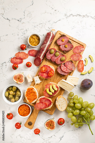 Assortment of sausages and cheese, salami camembert brie, grapes, baguette slices, olives, on white background.