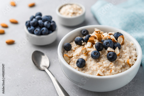 Oatmeal porridge in a bowl with blueberries and almonds on grey stone background. Concept of healthy breakfast, food, and lifestyle