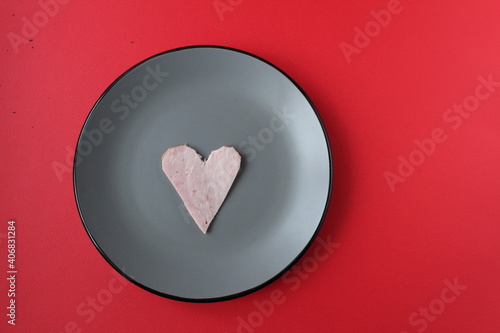 Still life breakfast for Valentine's Day Heart of ham sausage on a gray plate on a red bright background with a copy of the space