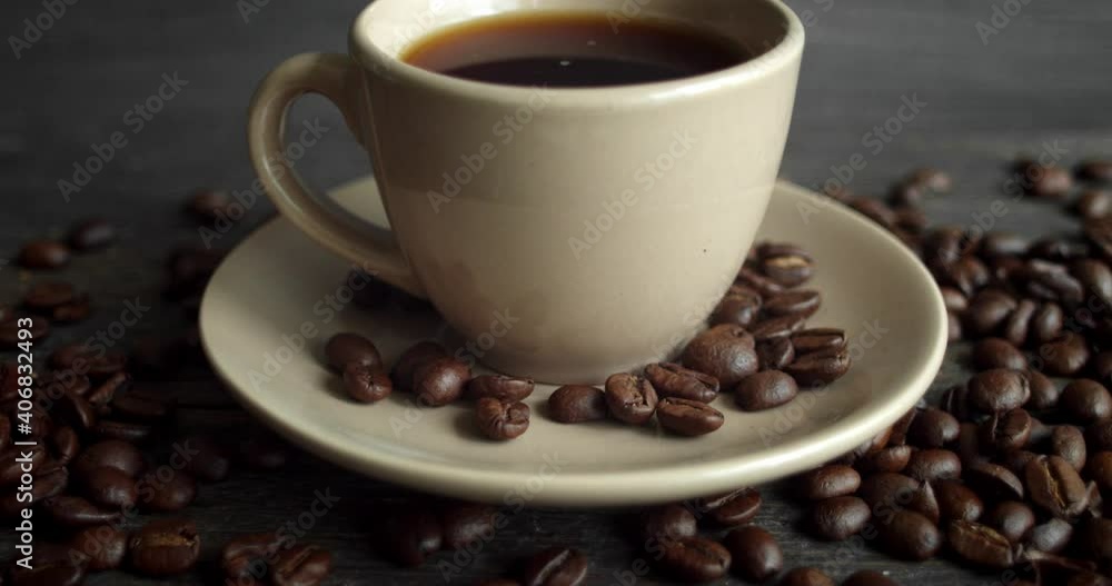 Cup of coffee with roasted coffee beans scattered on a wooden table. Mug of fresh black coffee. Fresh arabica roasted coffee beans. Great start of perfect morning. Espresso, americano, doppio. Cup of coffee with roasted coffee beans scattered on a wooden table. Mug of fresh black coffee. Fresh arabica roasted coffee beans. Great start of perfect morning. Espresso, americano, doppio.