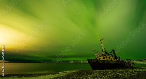 Abandoned boat on the Barents Sea beach in Teriberka, Russia. A cloudy sky illuminated by the northern lights.