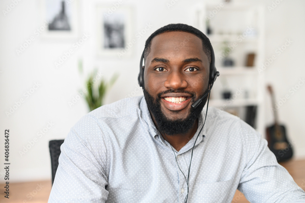 Smiling young African-American office worker wearing a headset and looking at the camera, a positive man with the beard working in the customer service department, making and receiving calls Smiling young African-American office worker wearing a headset and looking at the camera, a positive man with the beard working in the customer service department, making and receiving calls