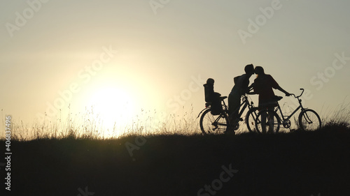 The newlyweds in love kiss with the child on the bicycles during the sunset.