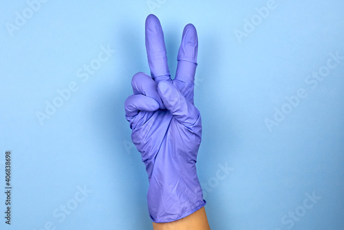 A female hand in a medical glove shows the gesture of victory.