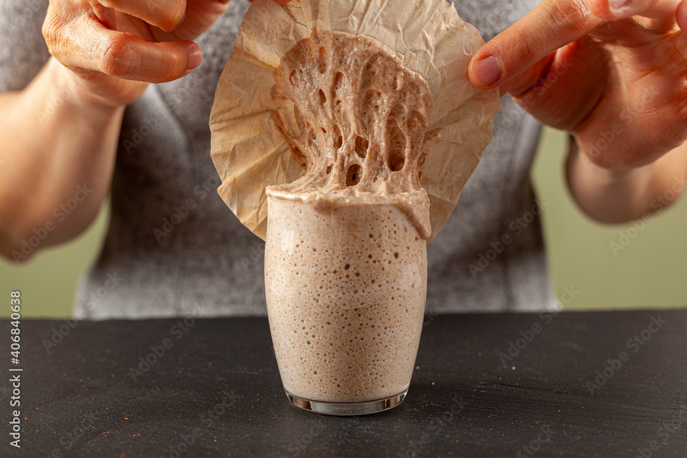 Ταπετσαρία A woman is carefully removing the top cover of a sourdough starter culture which is about to overflow the glass cup