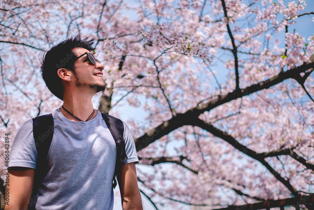 Young traveler with sunglasses standing under the sakura trees blooming in a park in Osaka, Japan Young traveler with sunglasses standing under the sakura trees blooming in a park in Osaka, Japan