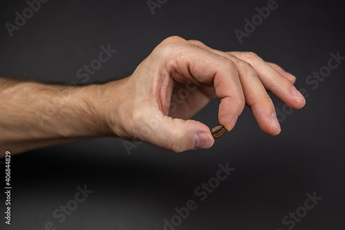 a mans hand holding a coffee bean above a dark colored table