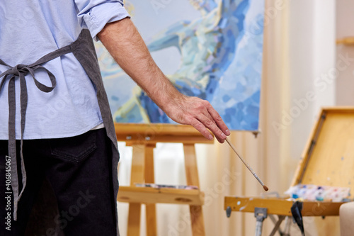 male painter in apron making masterpiece with brush on canvas, picture on easel. design, art, craft, painting concept