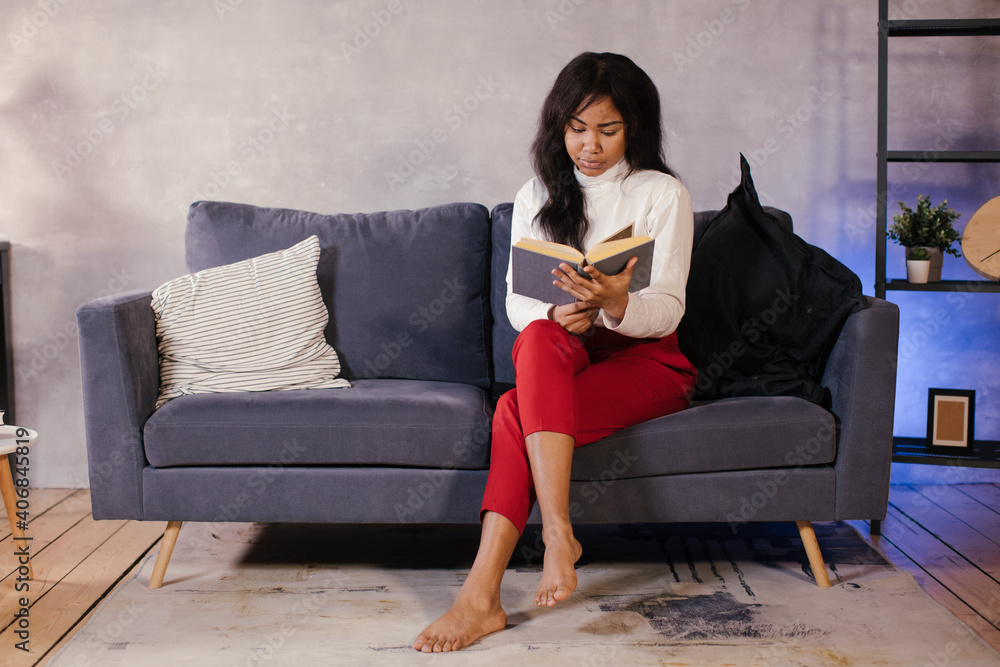 African girl reading a book on the sofa in her cozy room African girl reading a book on the sofa in her cozy room