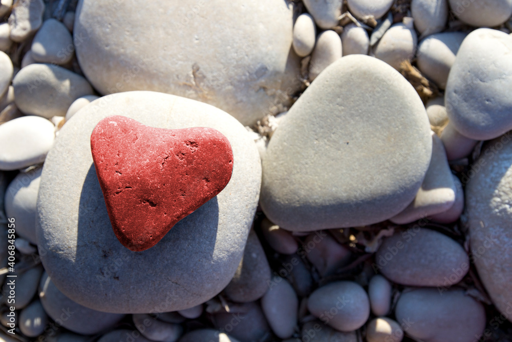 Obraz premium Red stone heart among river or sea pebble stones, Valentine's Day, perfect love