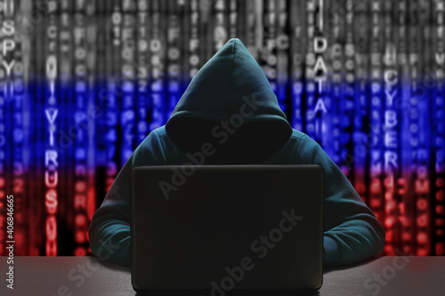Unknown Russian hacker in a hood against the background of a binary code in the color of the flag of Russia