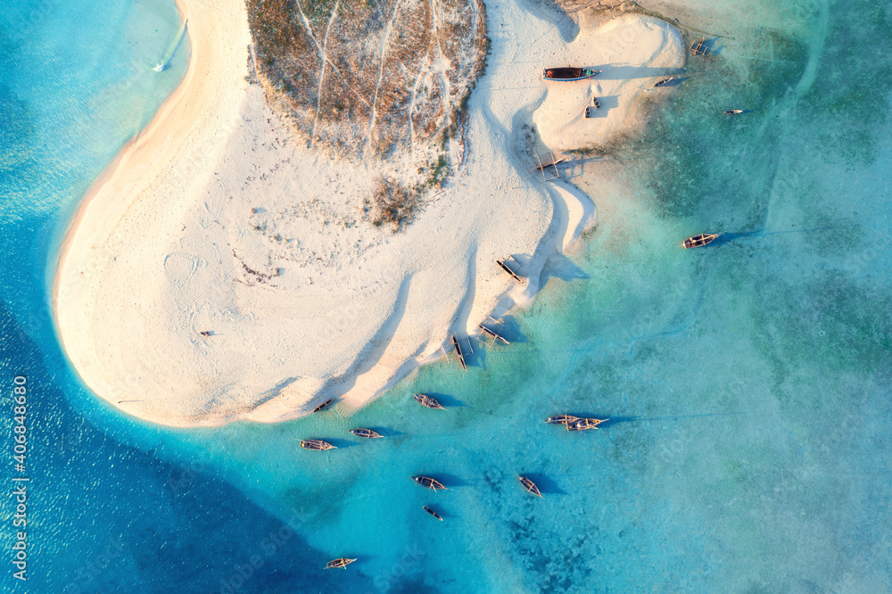 Aerial view of the fishing boats on tropical sea coast with white sandy beach at sunset. Summer travel in Zanzibar, Africa. Landscape with boats, yachts, green palm trees, clear blue water. Top view