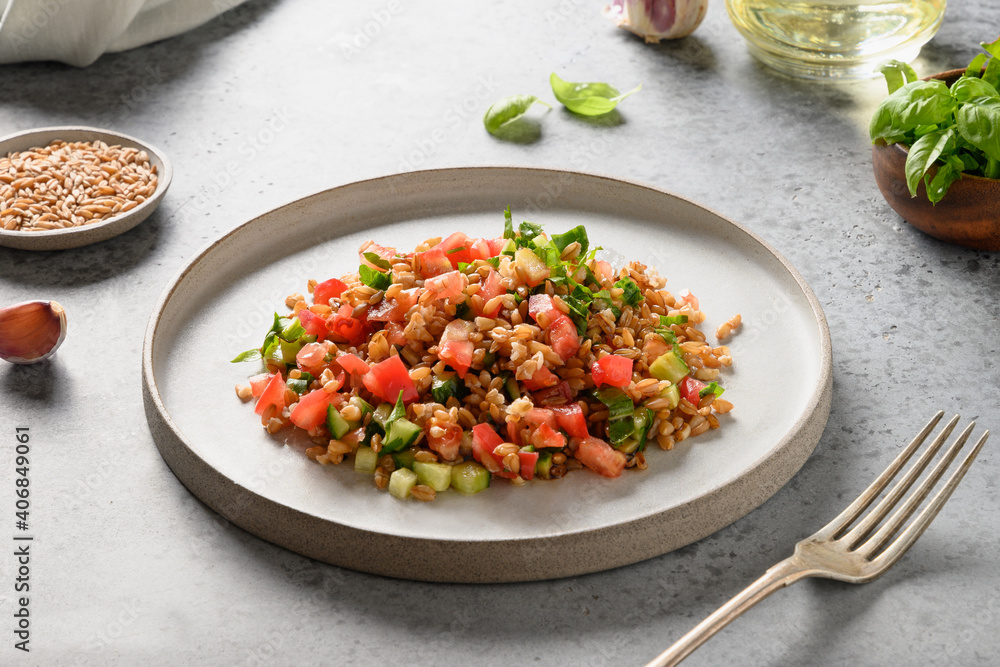 Useful vegan salad of whole grain cereal spelt with vegetables, tomato, cucumber, greens on grey. Close up. Useful vegan salad of whole grain cereal spelt with vegetables, tomato, cucumber, greens on grey. Close up.