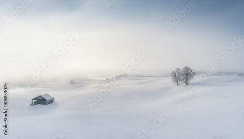 Dreamy winter landscape with snow covered trees, house and sun poking through mist