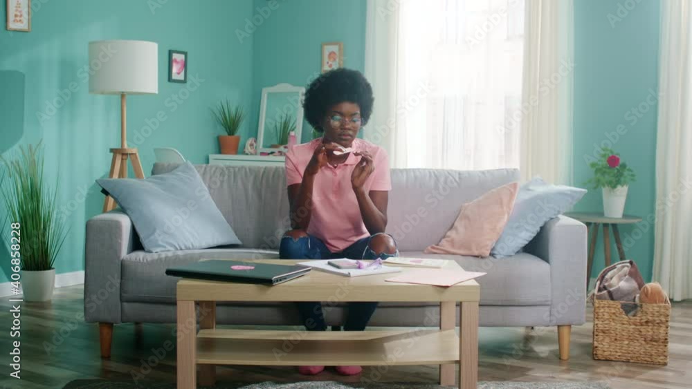 Young Afro-American woman is sitting on sofa at home and doing manicure, relaxing in cozy living room, beauty concept, Slow motion. Young Afro-American woman is sitting on sofa at home and doing manicure, relaxing in cozy living room, beauty concept, Slow motion.
