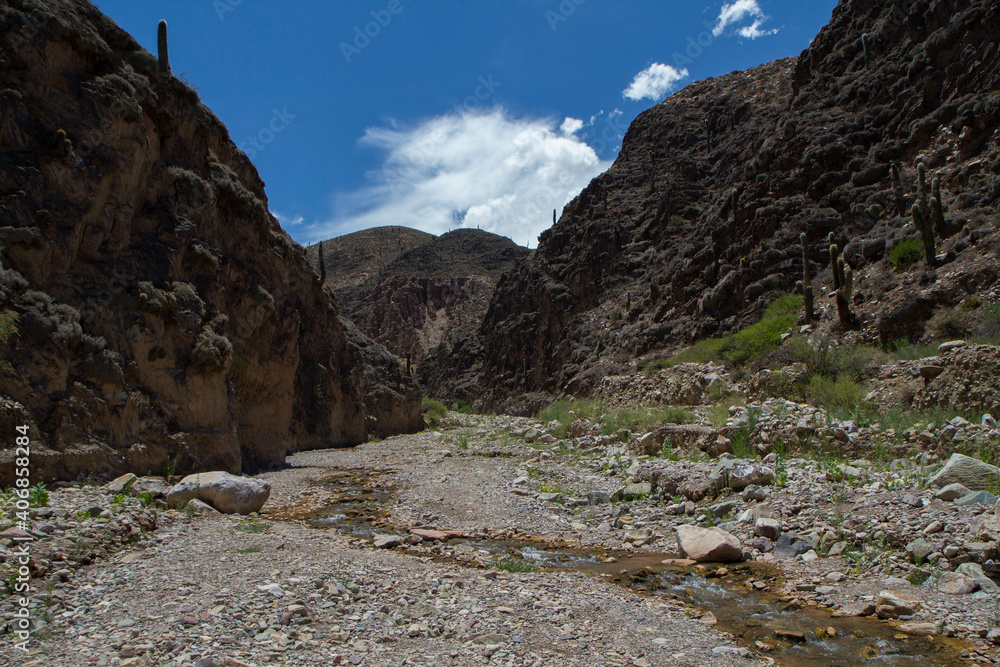 Arid landscape high in the Andes mountains. Panorama view of the stream and hiking path across the rocky mountains in a summer sunny day. 