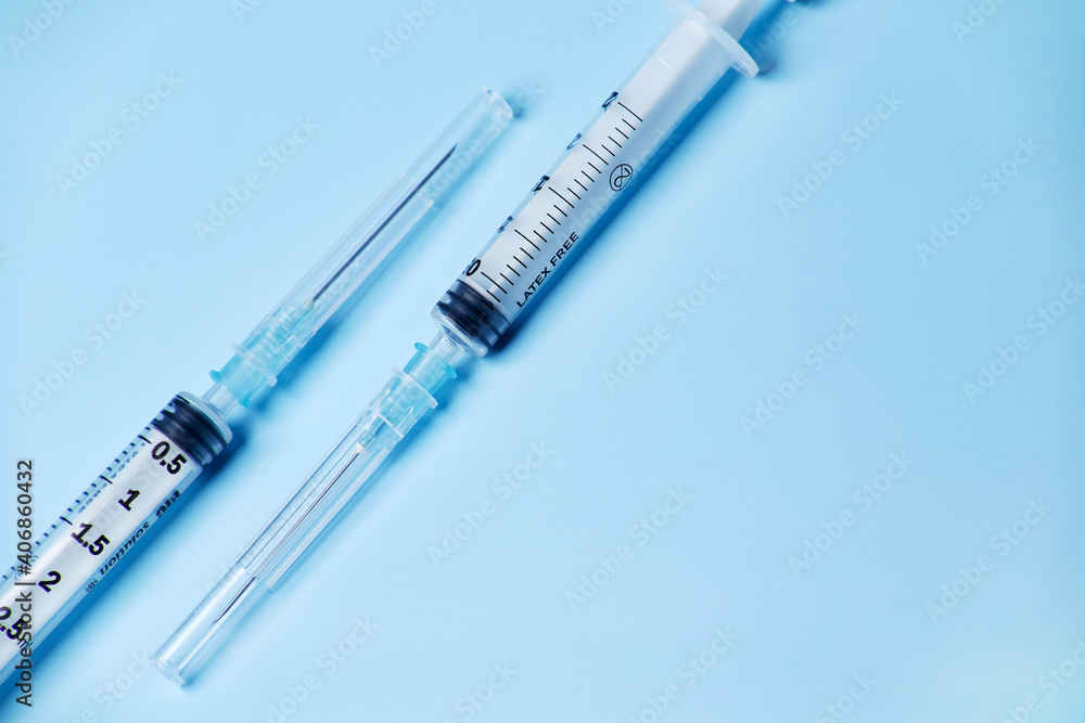 Two medical plastic disposable vaccination syringes with the needle in the cover cap isolated on the bright blue fond background Two medical plastic disposable vaccination syringes with the needle in the cover cap isolated on the bright blue fond background